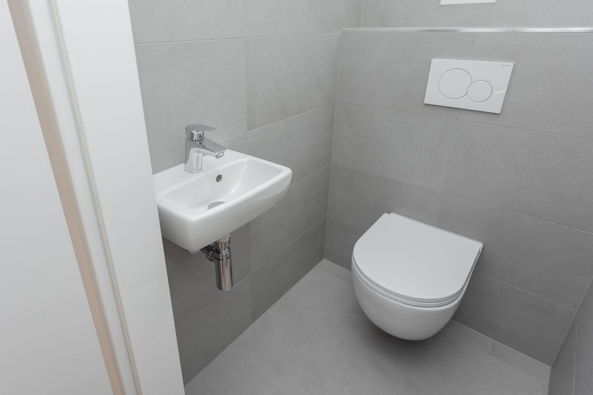 Detailansicht des modernen Gäste-WCs mit Wand-WC und kleinem Handwaschbecken, in Grau gehalten.