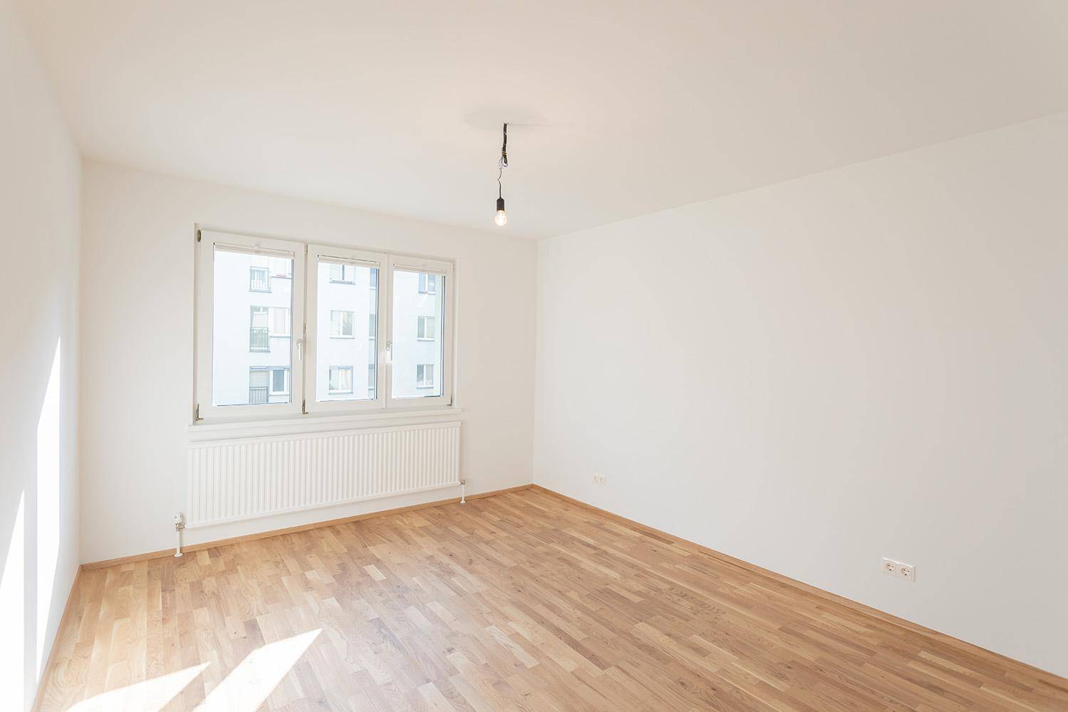Geräumiger, heller Raum mit Parkettboden und großem Fenster, ideal für Schlaf- oder Arbeitszimmer.