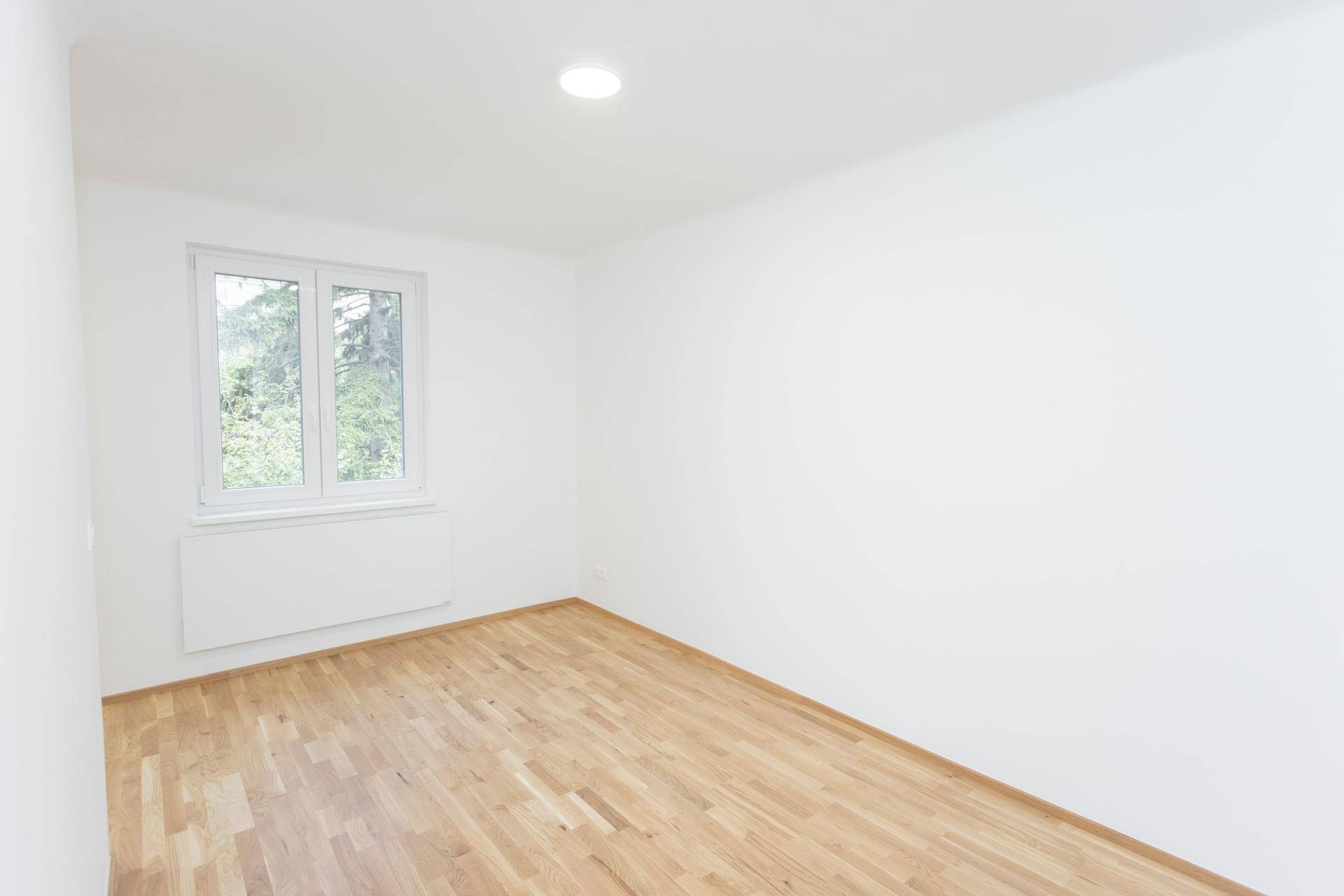 Heller, leerer Raum mit Holzfußboden und Fenster mit Blick ins Grüne.