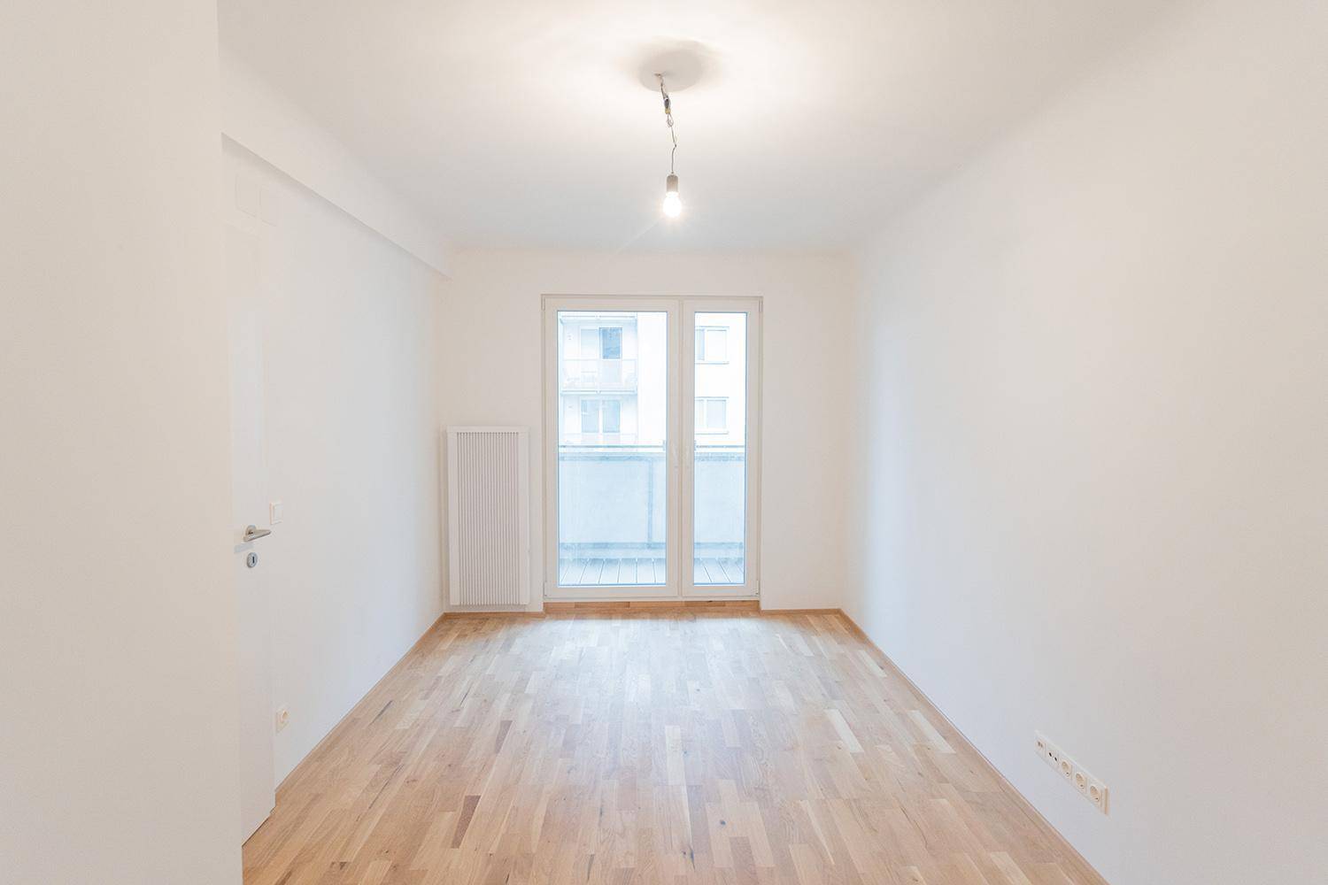 Geräumiges Zimmer mit Parkettboden und großen Fenstertüren, die auf einen Balkon führen.