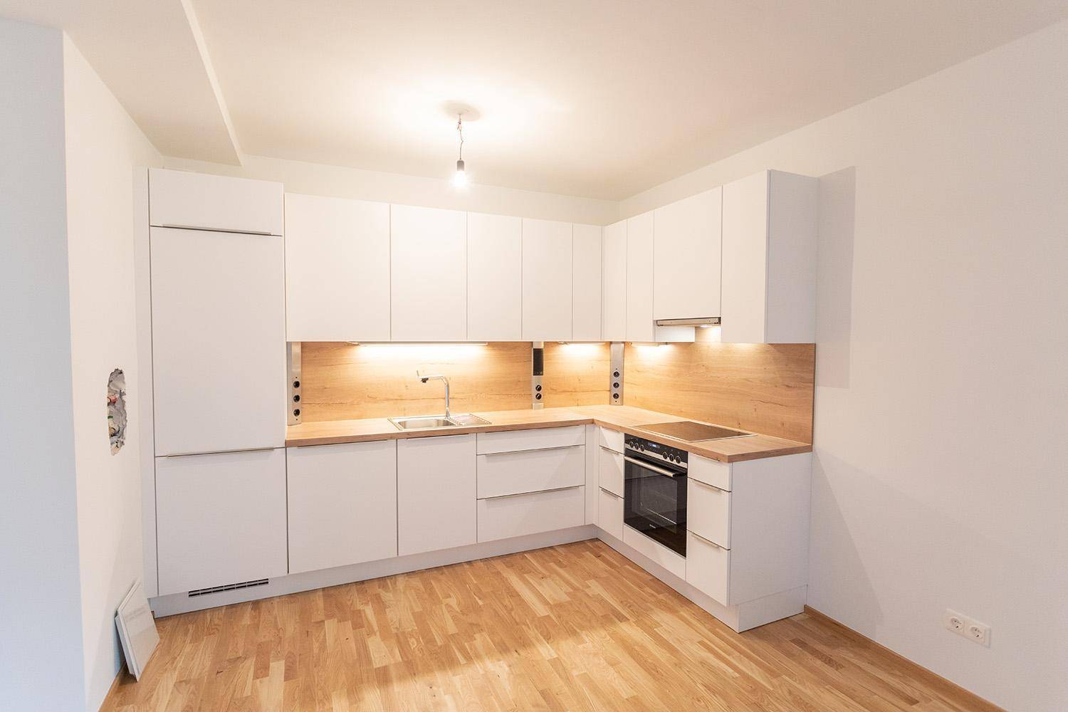 Neue Einbauküche mit weißen Schränken, Holzdetails und Herd, bereit zur Nutzung.