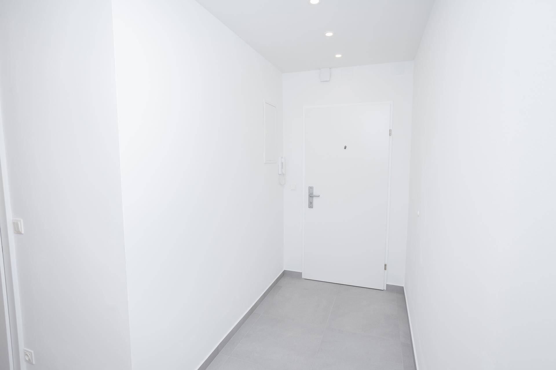 Eingangsbereich des Flurs mit grauen Fliesen, weißen Wänden und der modernen Wohnungstür.