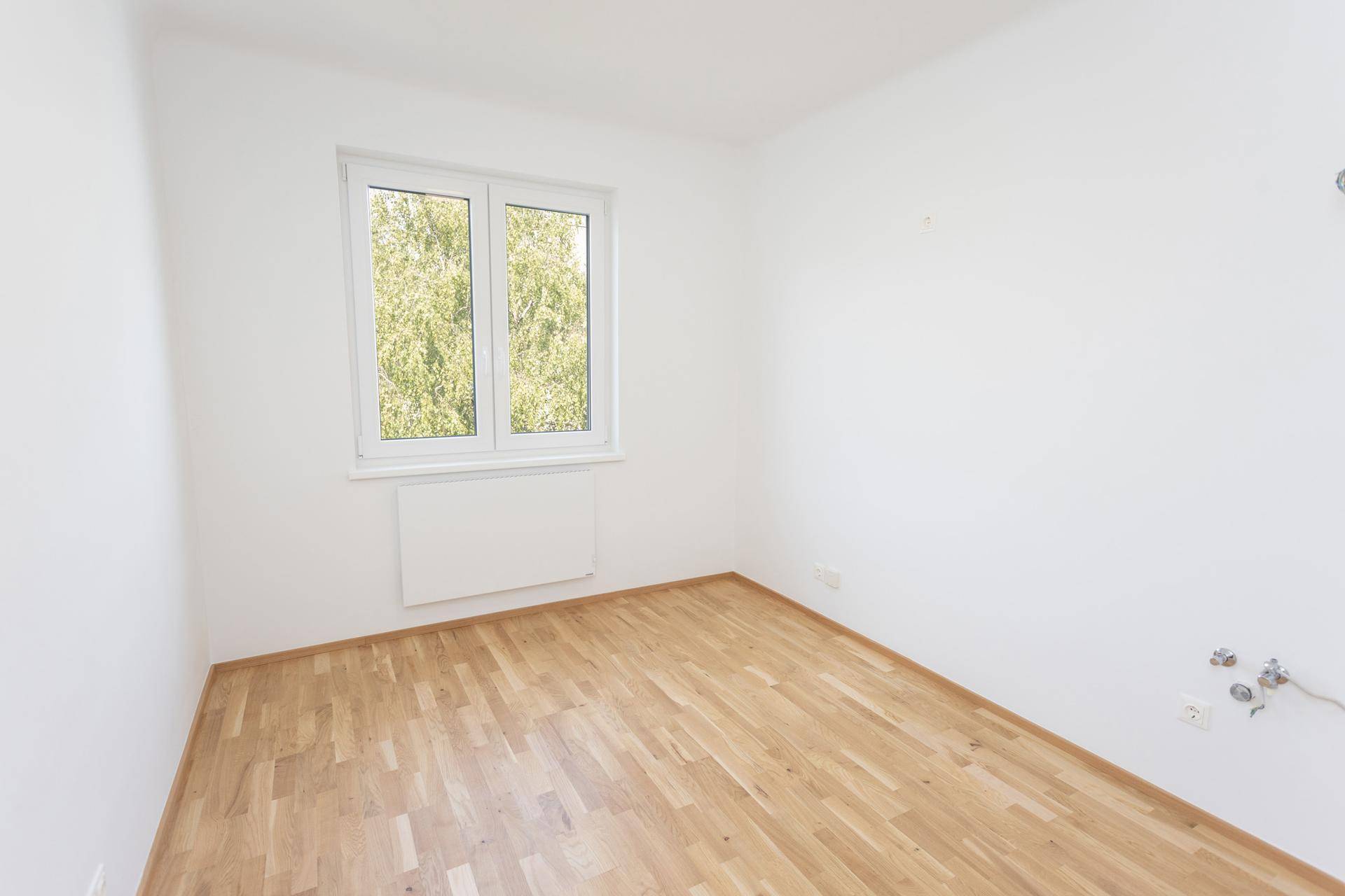 Helles, leeres Zimmer mit Parkettboden und Fenster, vielseitig nutzbar für verschiedene Zwecke.