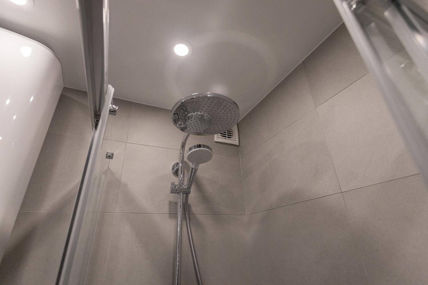 Detailaufnahme der modernen Regendusche mit integriertem Abluftventilator in der Decke.