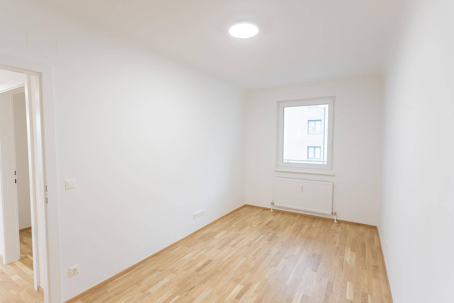 Leeres Zimmer mit hellem Parkettboden und weiß gestrichenen Wänden, bereit zur individuellen Gestaltung.
