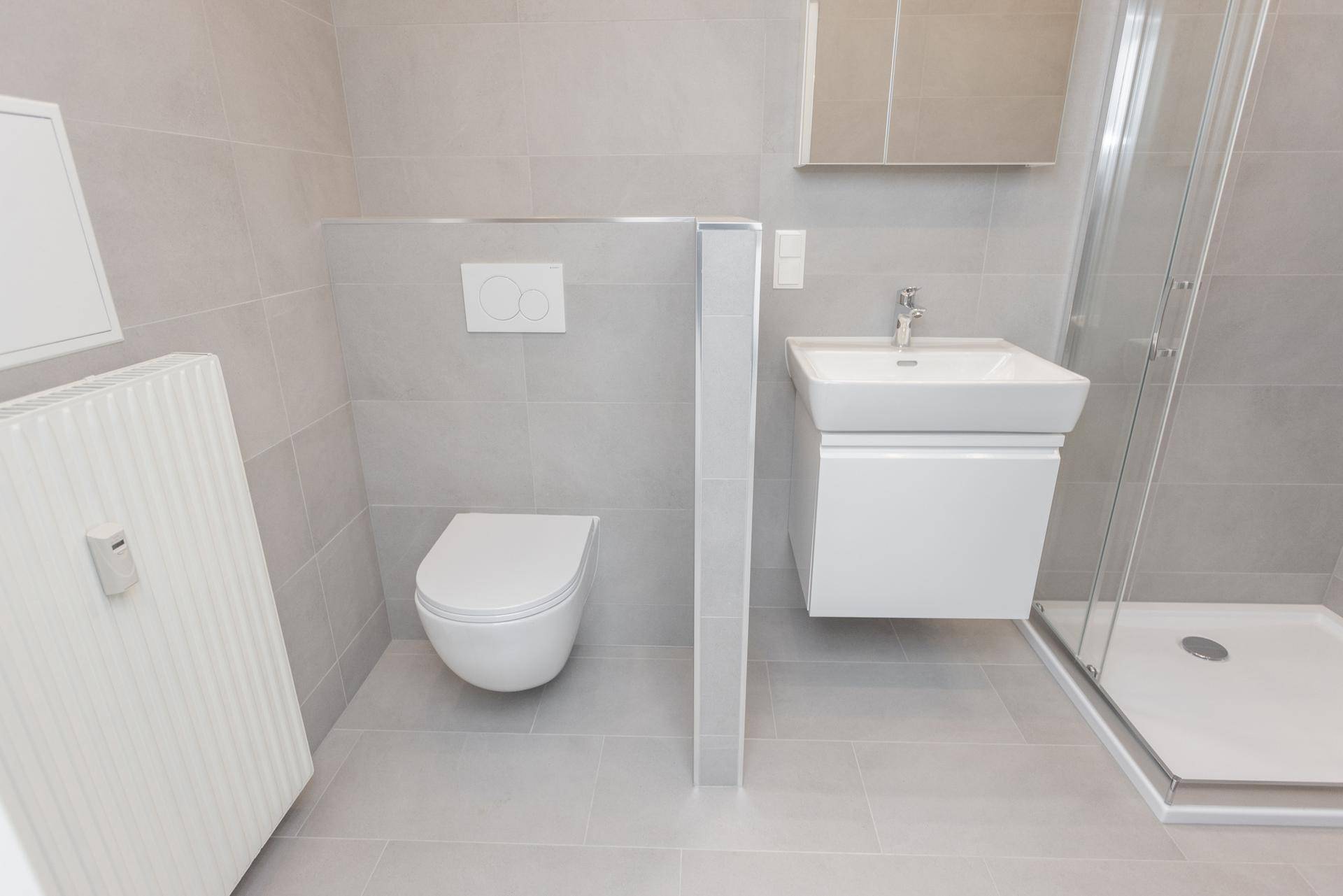 Modernes Badezimmer mit grauen Fliesen, wandhängender Toilette, Waschbecken und Duschkabine.