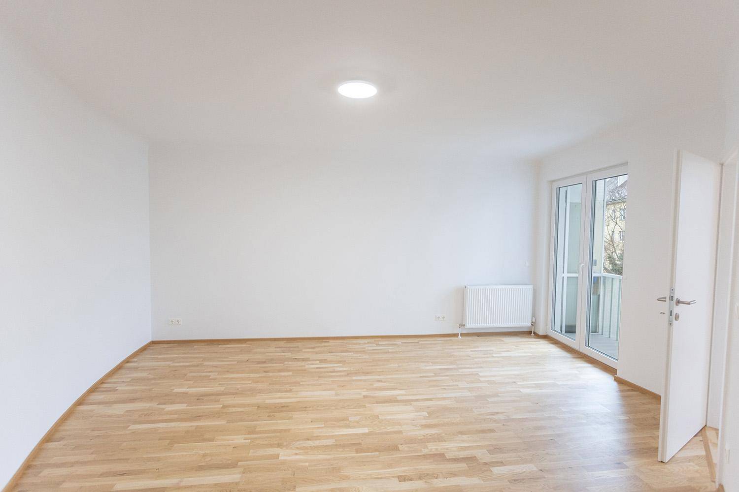 Heller Wohnraum mit Holzboden, Heizkörper und Zugang zu einem französischen Balkon.