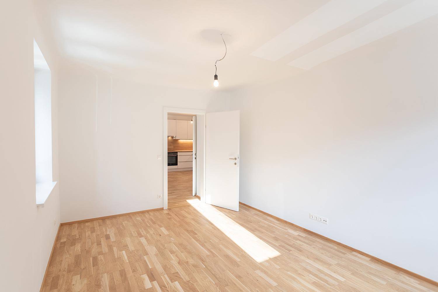 Heller Raum mit Parkettboden und Blick in eine moderne, offene Küche.