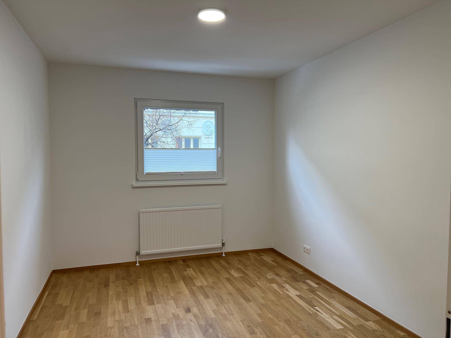 Leeres Zimmer mit hellem Holzboden, weiß gestrichenen Wänden und Fenster mit Ausblick.