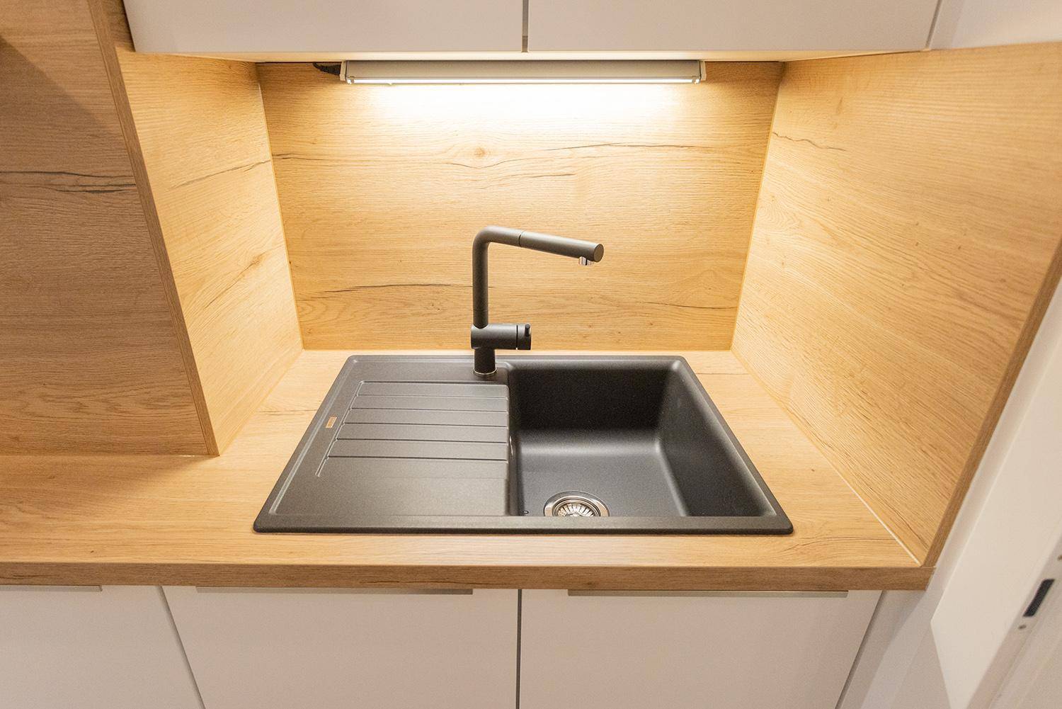Detailansicht der modernen schwarzen Spüle mit Armatur und Holzoptik-Rückwand in der Küche.