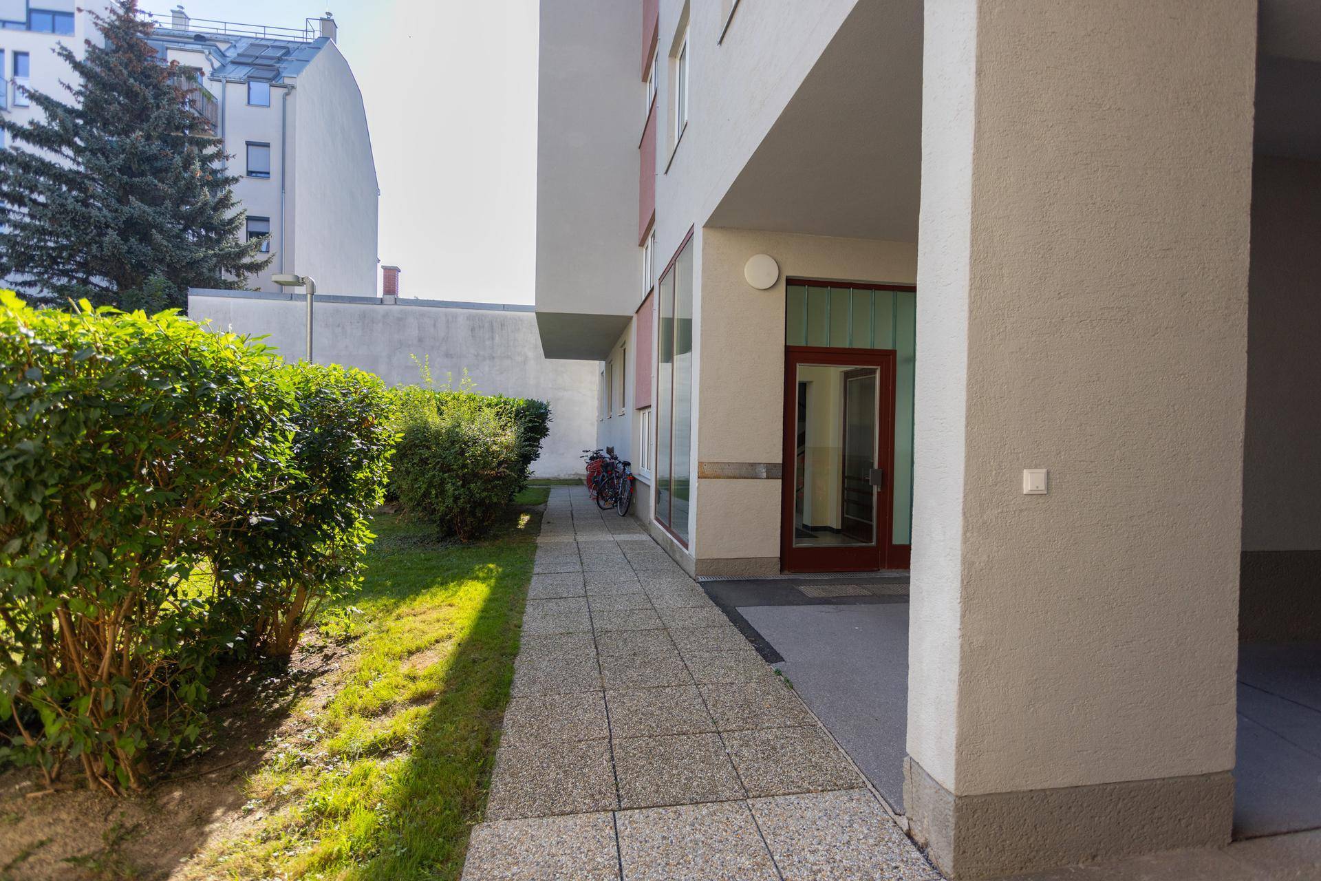 Gepflegter Außenbereich mit Gehweg, grünen Hecken und Rasenfläche neben dem Gebäude.