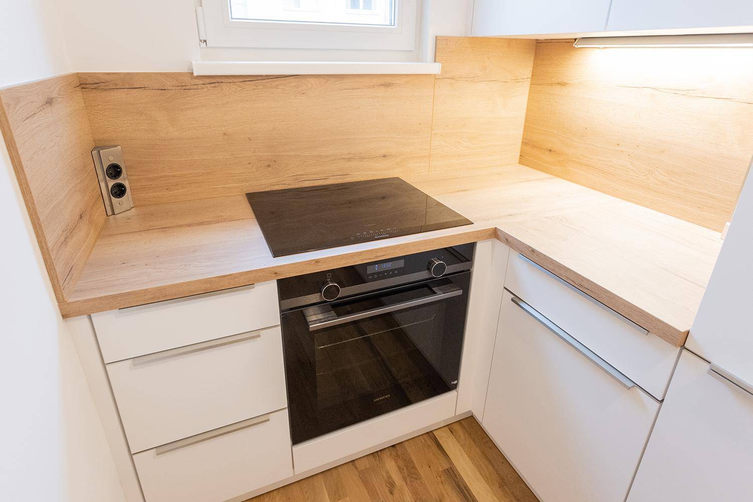 Detailaufnahme des Induktionskochfelds und Backofens mit Holzoptik-Arbeitsplatte in der Küche.