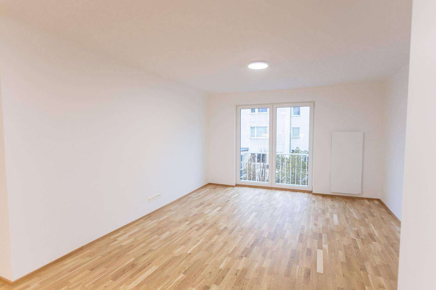 Geräumiges, helles Zimmer mit Holzboden und Fensterfront zum Balkon, ideal für individuelle Gestaltung.