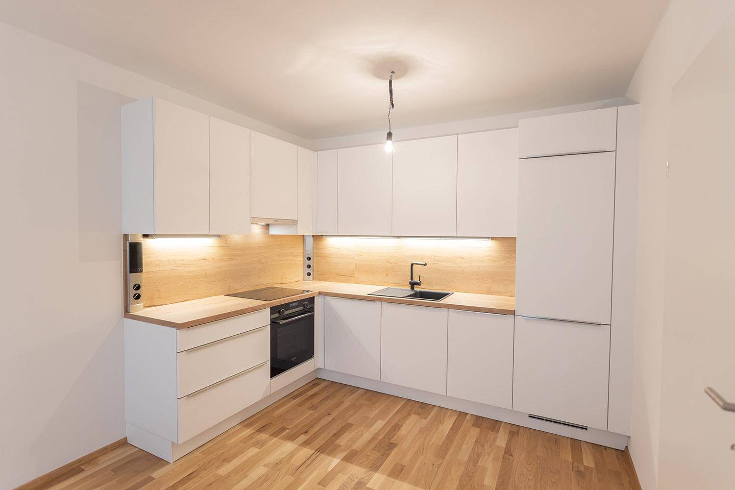 Moderne weiße Einbauküche mit Holzarbeitsplatte, Induktionskochfeld und integrierten Geräten.
