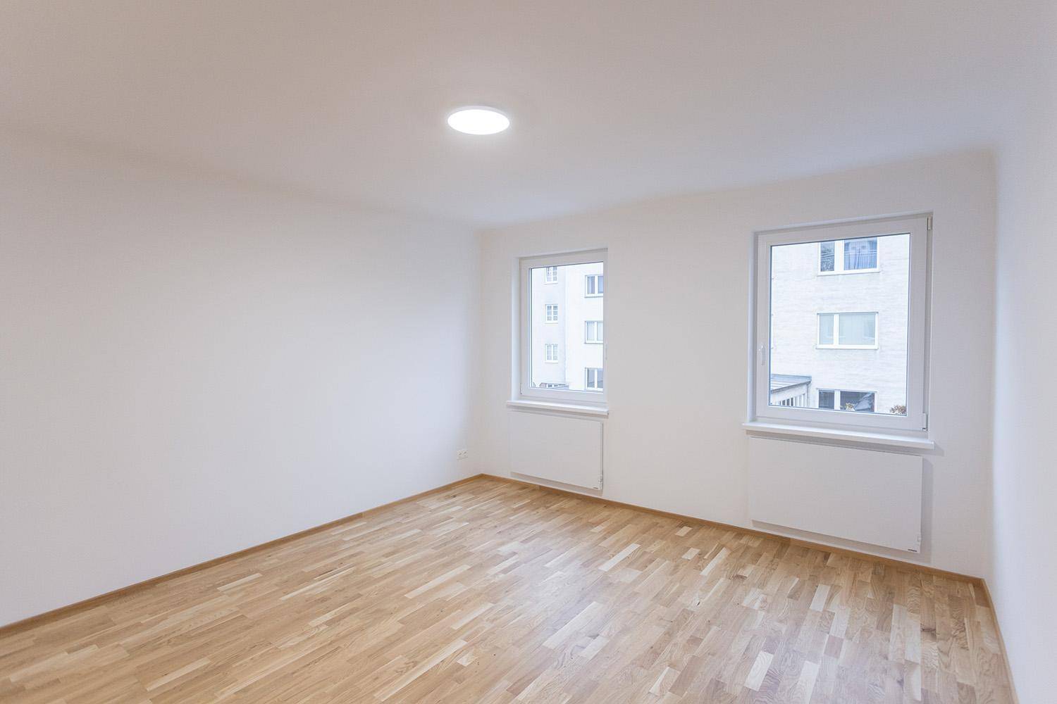 Geräumiges, helles Zimmer mit Holzboden und zwei Fenstern, ideal als Schlafzimmer.