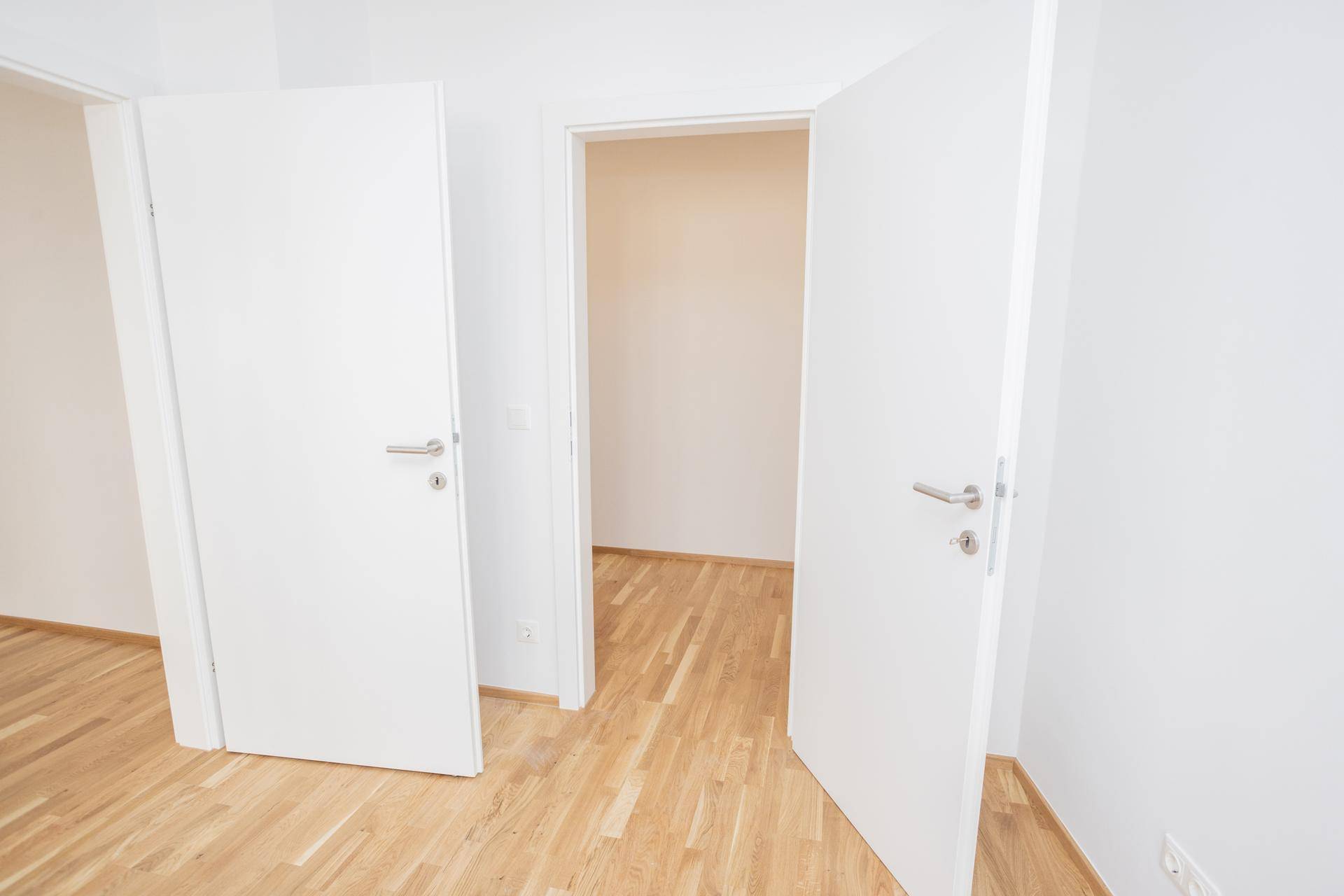 Heller Flur mit mehreren weißen Türen und einem warmen Holzparkettboden, der zu verschiedenen Räumen führt.