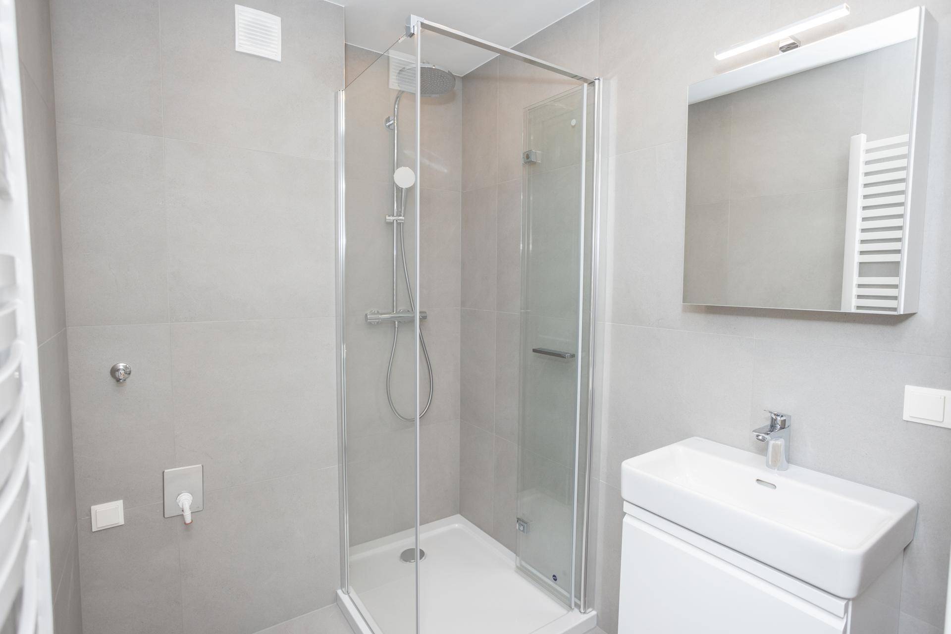 Helles Badezimmer mit Duschkabine, modernem Waschbecken und Spiegelschrank, alles in Grautönen gehalten.