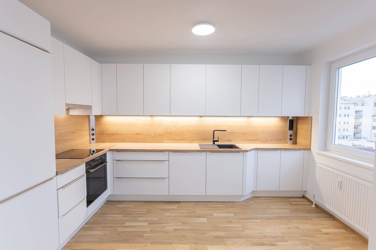 Helle, moderne Küche mit weißen Fronten, Holz-Arbeitsplatte und Fensterblick.