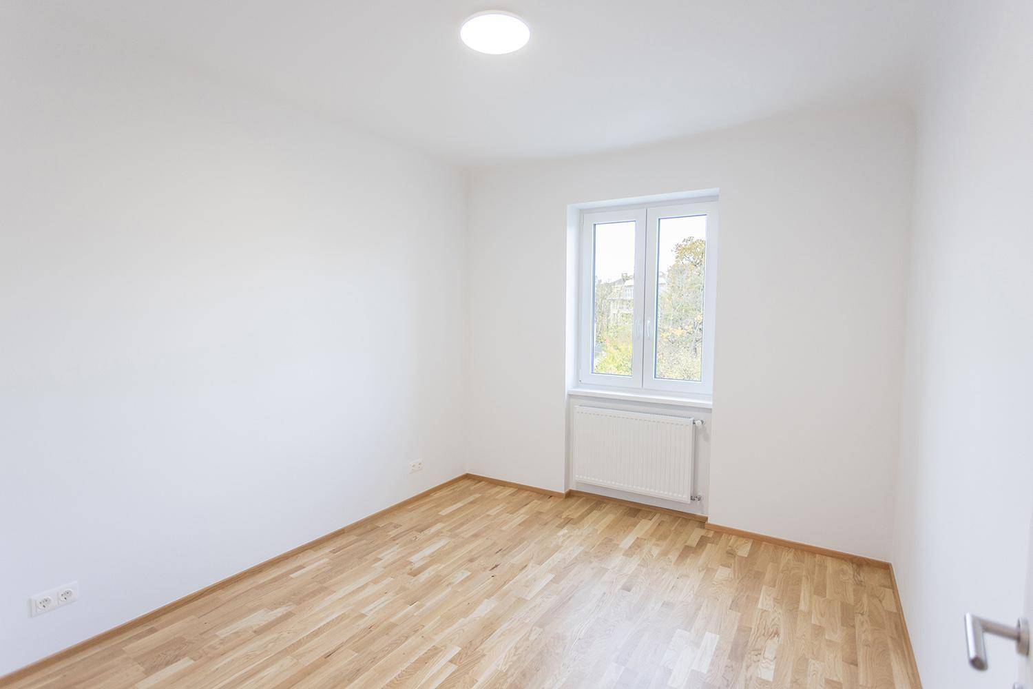 Helles Schlafzimmer mit Holzparkett, weißen Wänden und Fenster, unmöbliert.