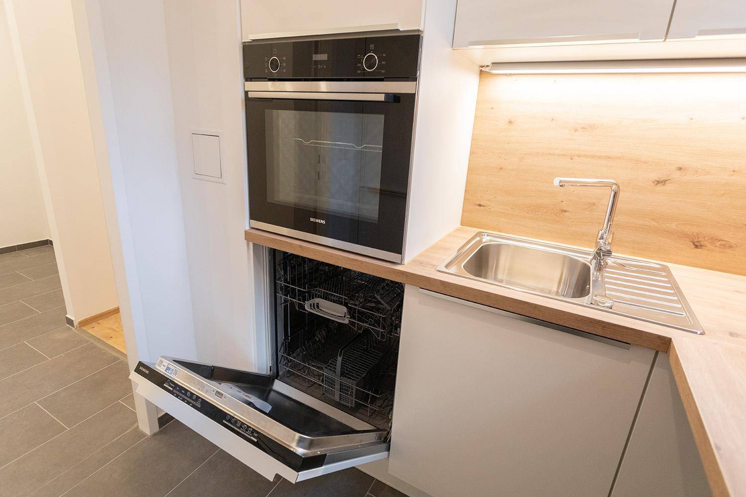 Moderne Küche mit weißen Schränken, Holzarbeitsplatte, Spüle, Backofen und offenem Geschirrspüler.