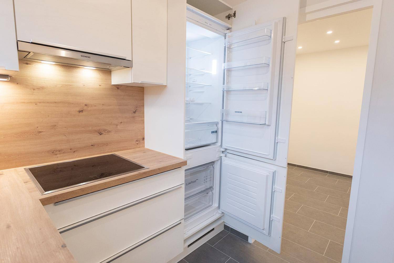 Moderne Küche mit weißen Schränken, Holzarbeitsplatte, Induktionskochfeld und offenem Kühlschrank.