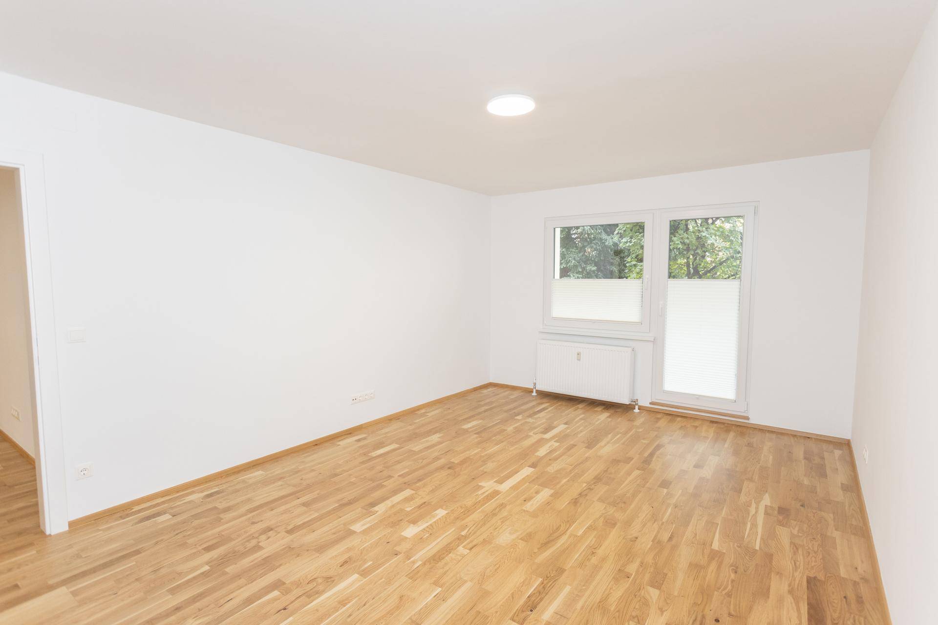 Helles Zimmer mit Parkettboden und großem Fenster, das viel Tageslicht hereinlässt.