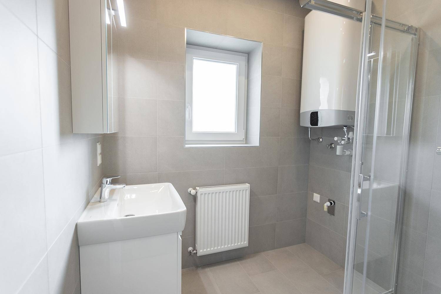 Modernes Badezimmer mit grauen Fliesen, Dusche, Waschbecken und Fenster.