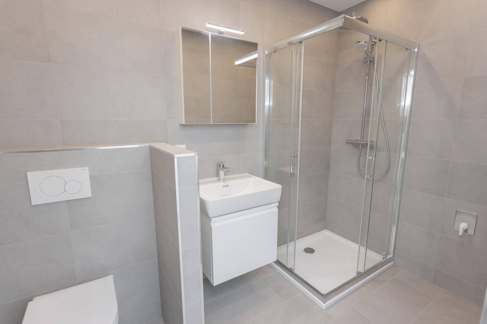 Modernes Badezimmer mit Duschkabine, Waschbecken, Spiegelschrank und grauen Wand- und Bodenfliesen.