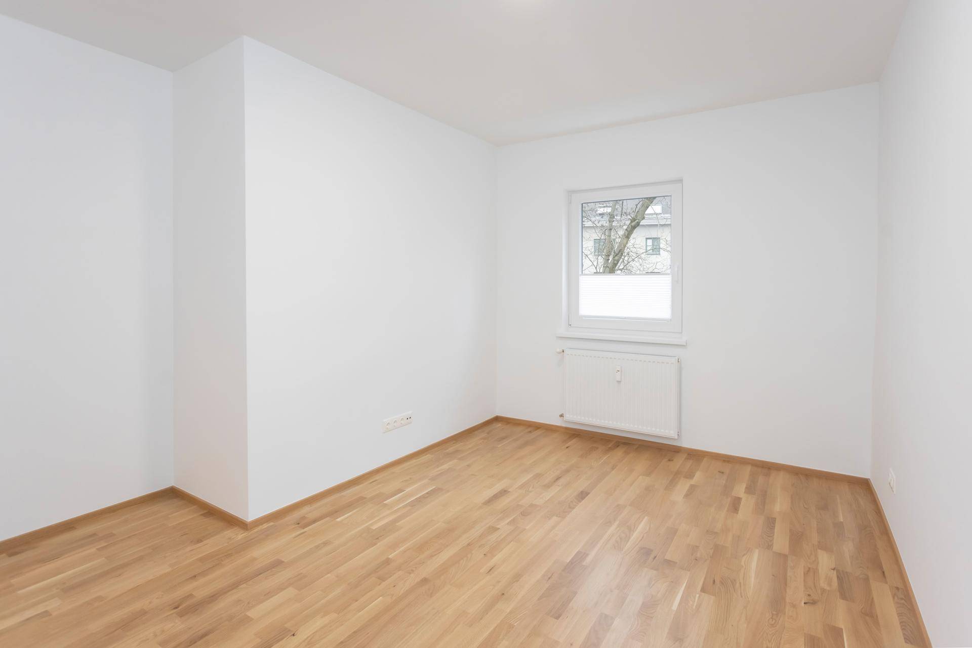 Leeres Schlafzimmer mit hellem Parkettboden und einem Fenster für viel Tageslicht.