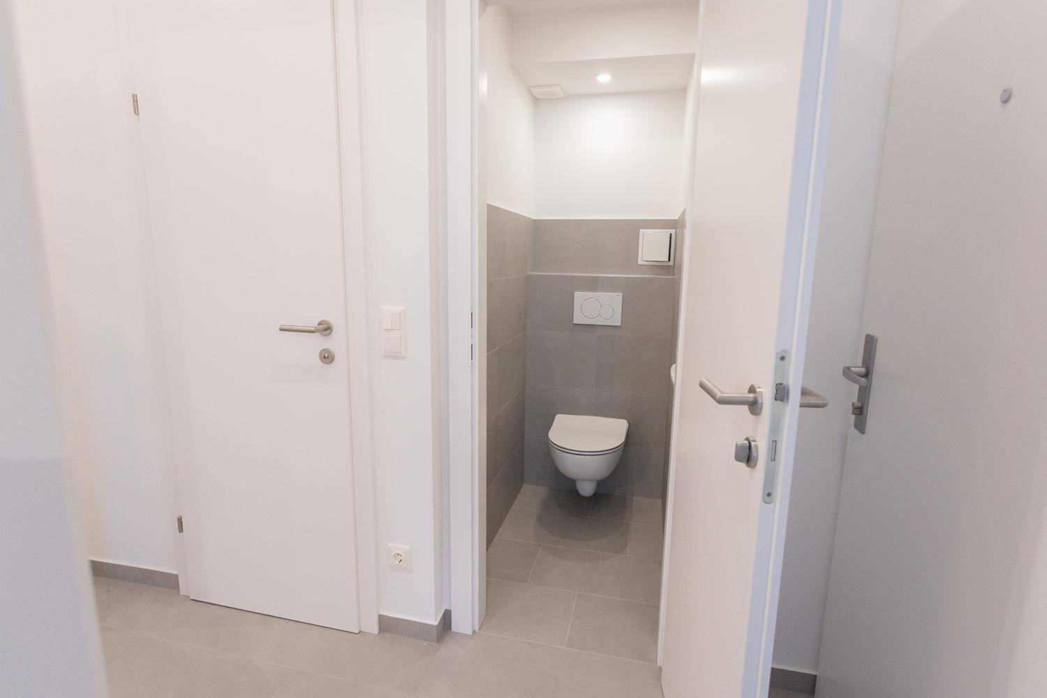 Modernes Gäste-WC mit wandhängender Toilette und eleganten grauen Fliesen.