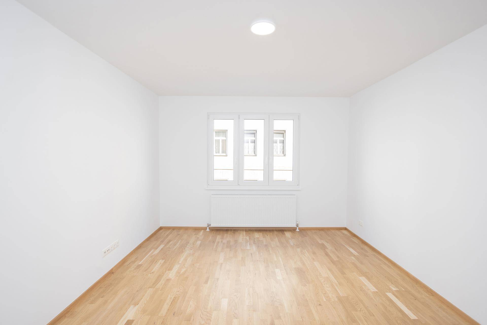 Helles und freundliches Zimmer mit Parkettboden und einem großen Fenster, das den Raum erhellt.