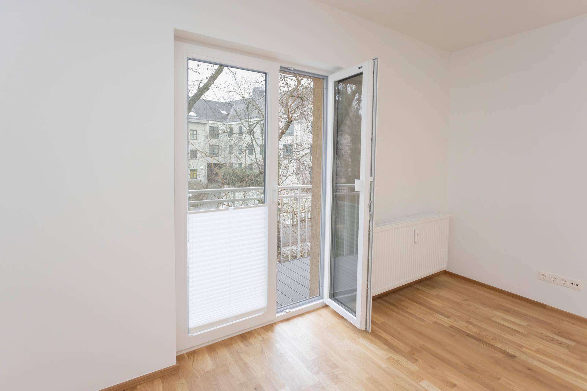 Heller Raum mit Parkettboden und Zugang zu einem Balkon, bietet viel Tageslicht.