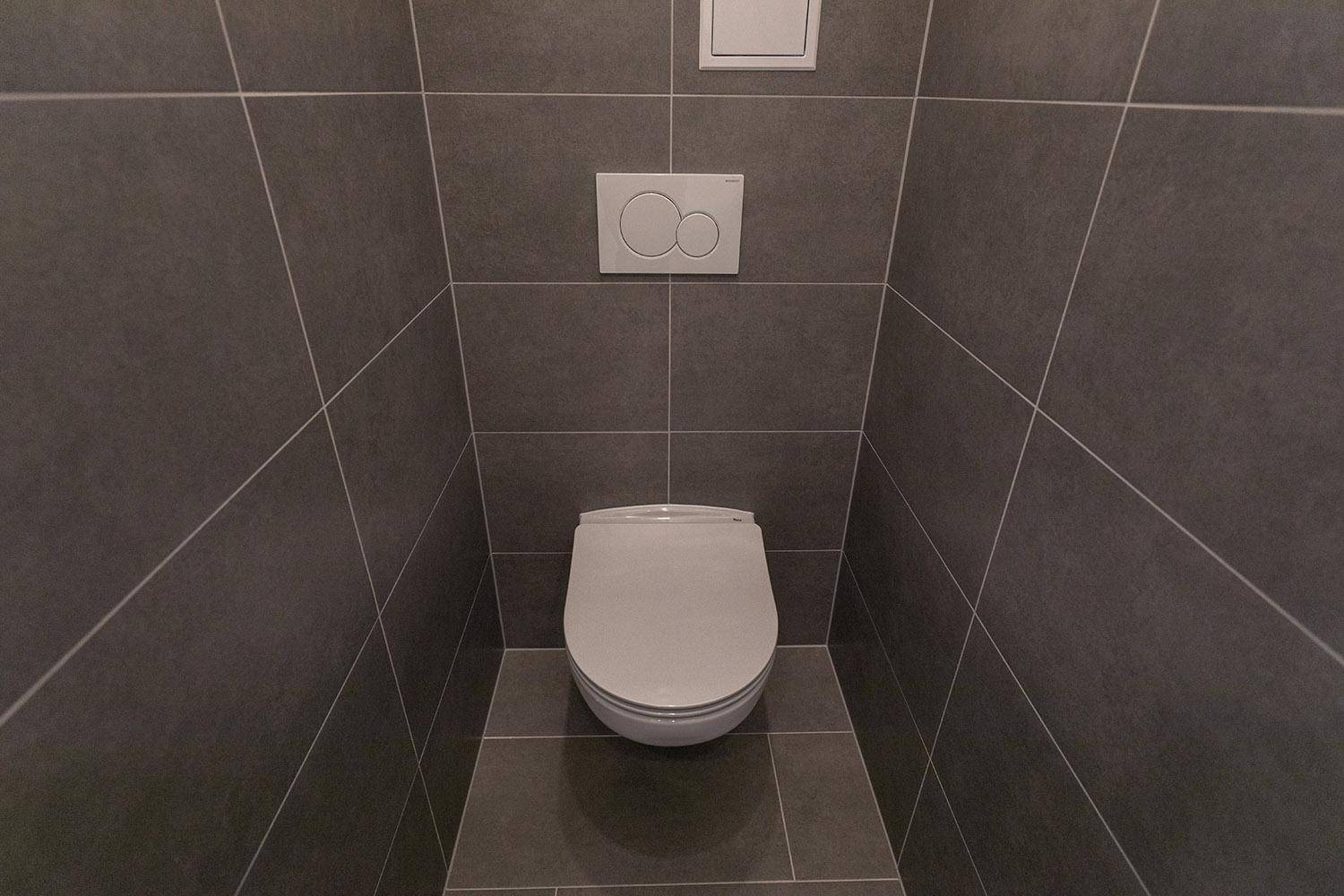 Modernes separates WC mit grauen Wand- und Bodenfliesen und wandhängendem WC.
