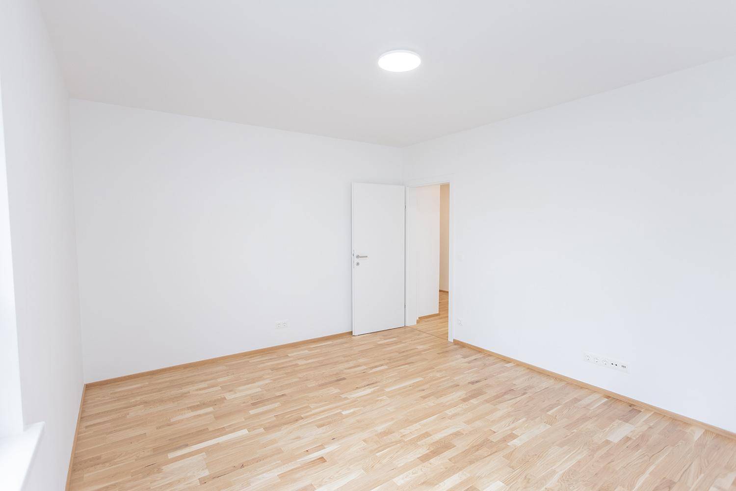 Heller Raum mit Holzparkettboden und weißen Wänden, bereit für individuelle Gestaltung.