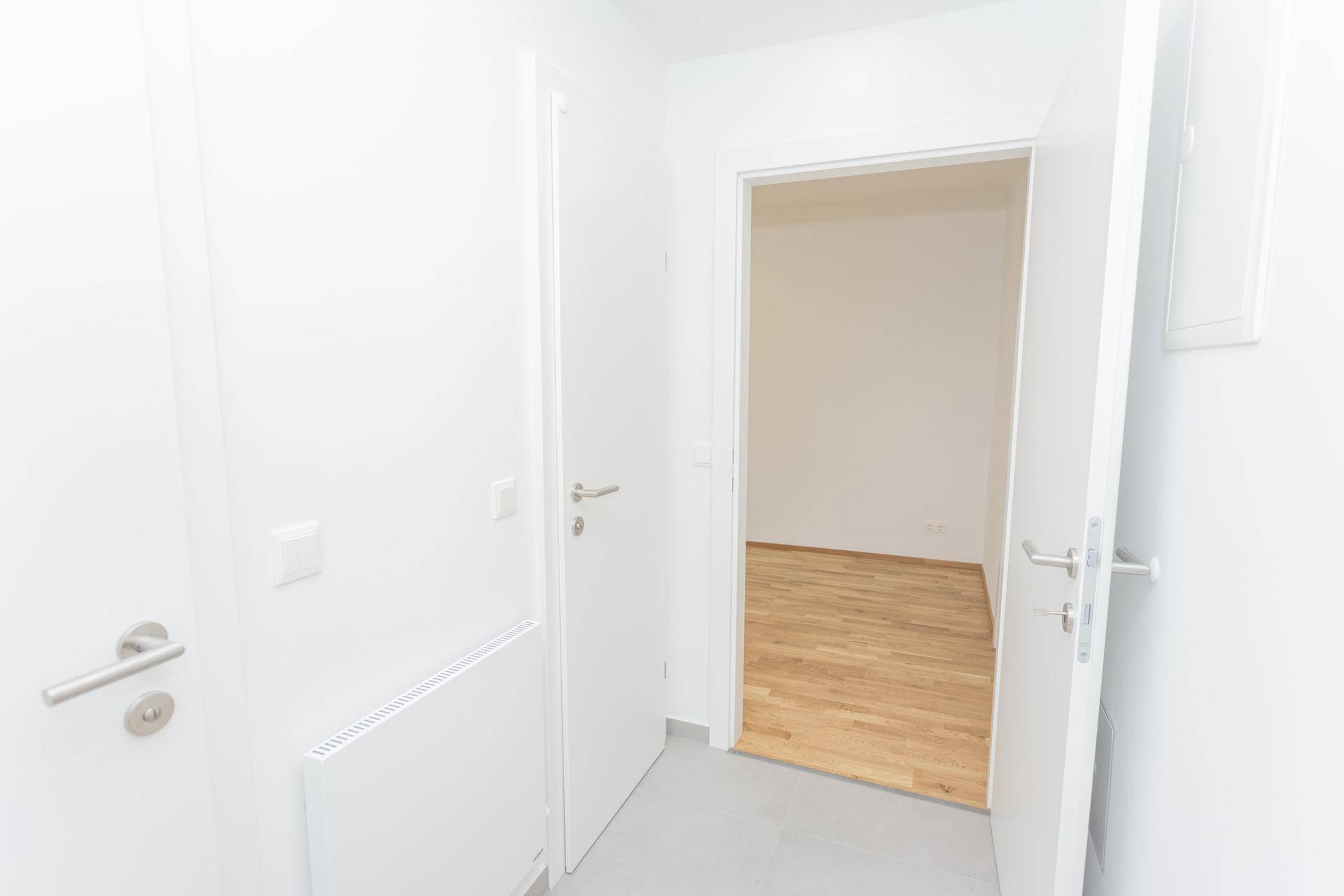 Flur mit hellem Fliesenboden, der in einen Raum mit Holzfußboden übergeht.