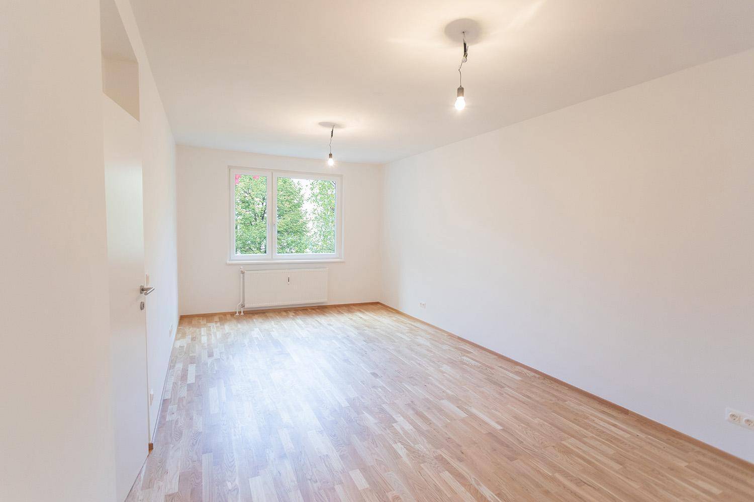 Geräumiges, leeres Zimmer mit Holzboden und zwei Fenstern, bereit zur Einrichtung.
