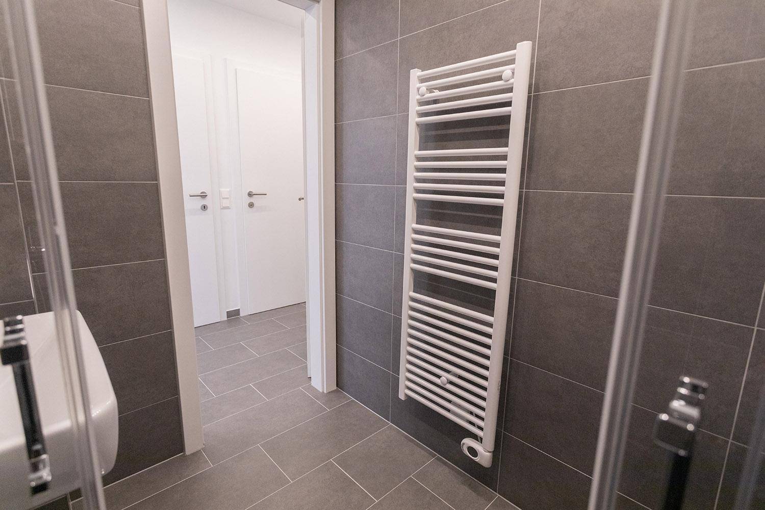 Beheizter Handtuchhalter in einem modern gefliesten Badezimmer mit Dusche.