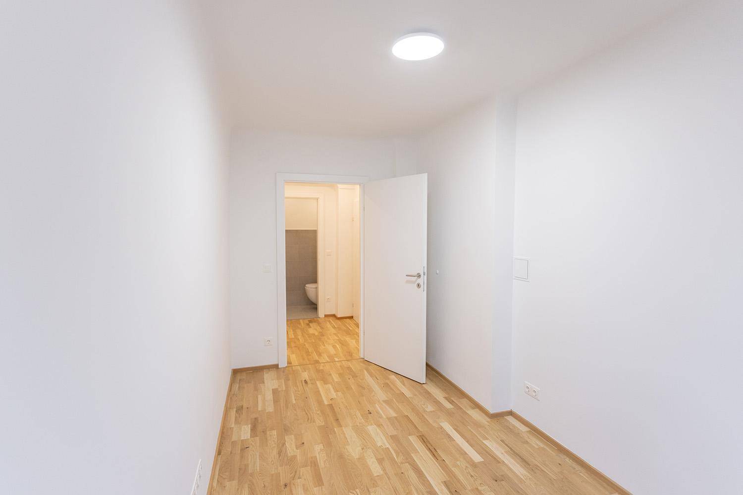 Helles Zimmer mit Holzboden und offener Tür, die den Blick auf die Gästetoilette freigibt.