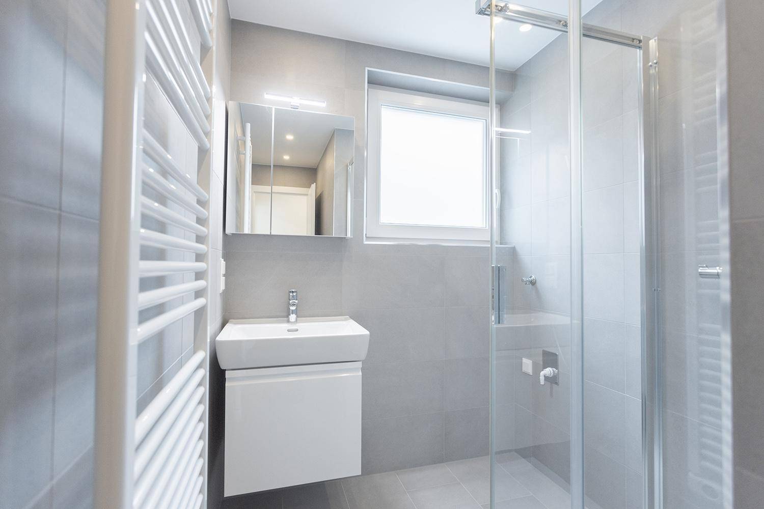 Modernes Badezimmer mit Dusche, Waschbecken, Spiegel und beheiztem Handtuchhalter.