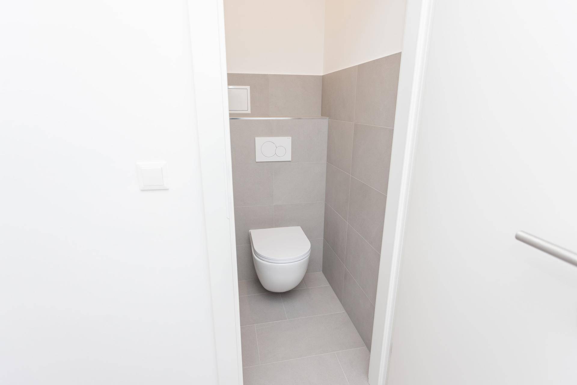 Modernes Gäste-WC mit wandhängender Toilette und grauen Fliesen an Wänden und Boden.