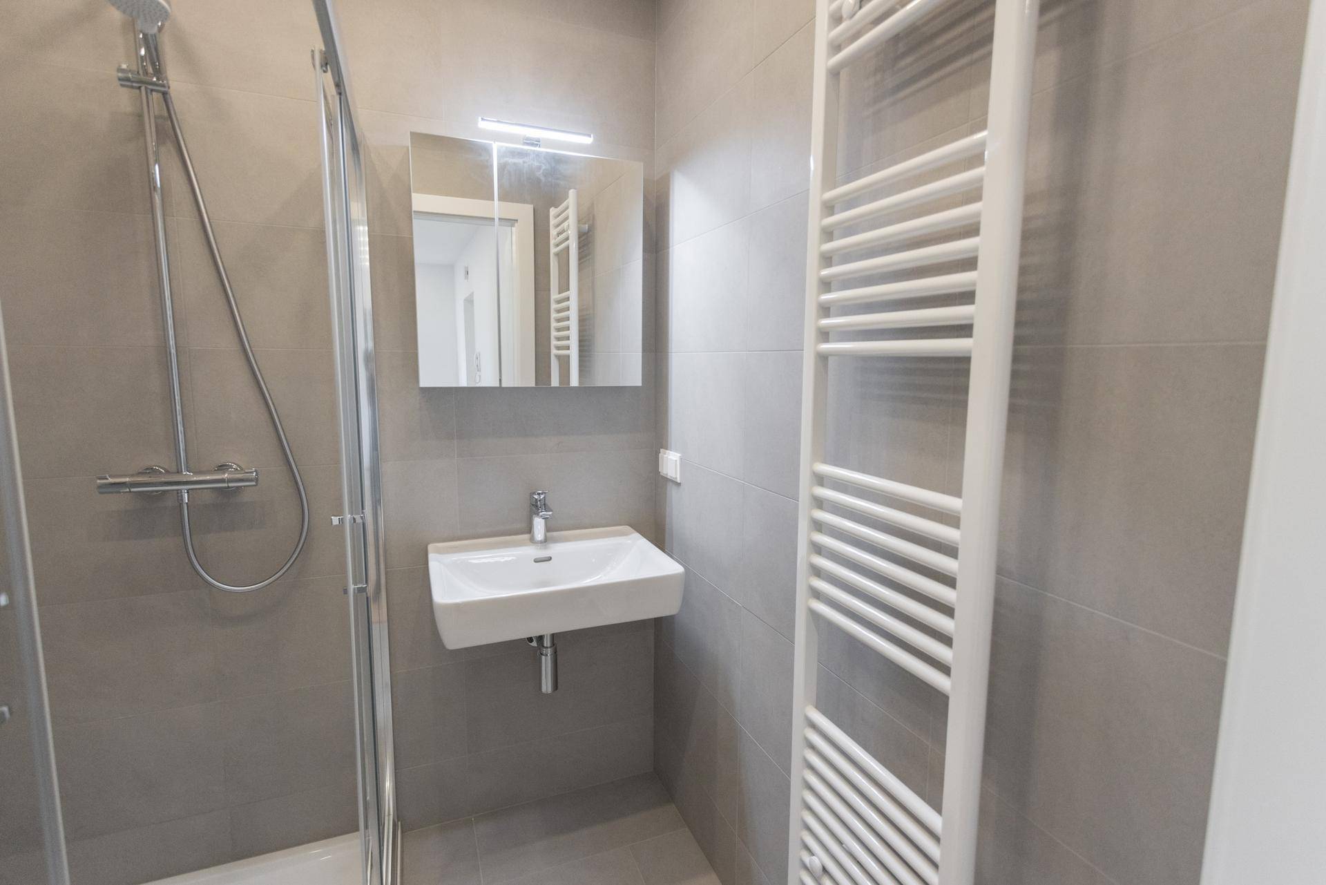 Modernes Badezimmer mit Dusche, Waschbecken, Spiegel und beheiztem Handtuchhalter in Grautönen.