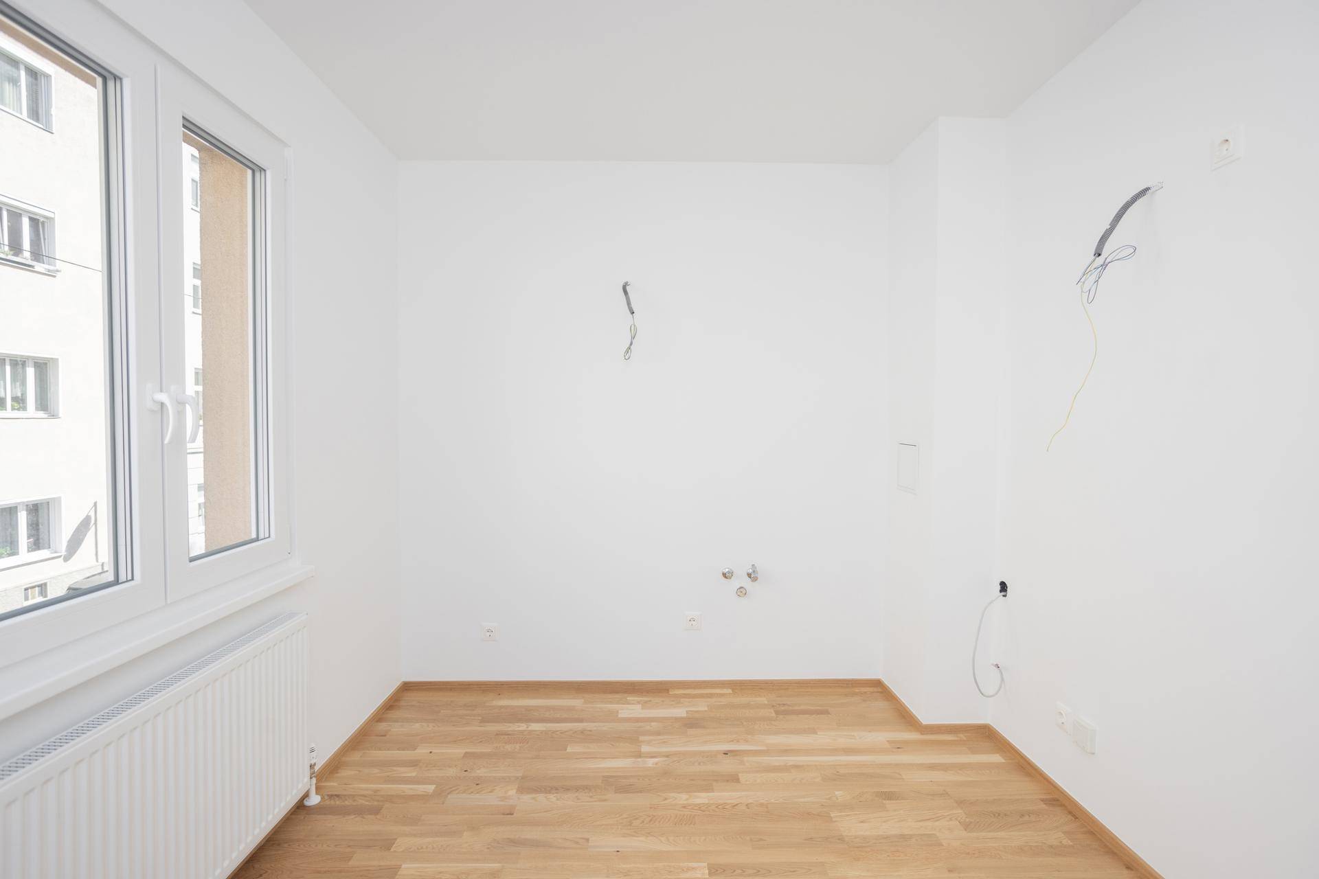 Geräumiges, leeres Zimmer mit Parkettboden und viel Tageslicht durch das große Fenster.