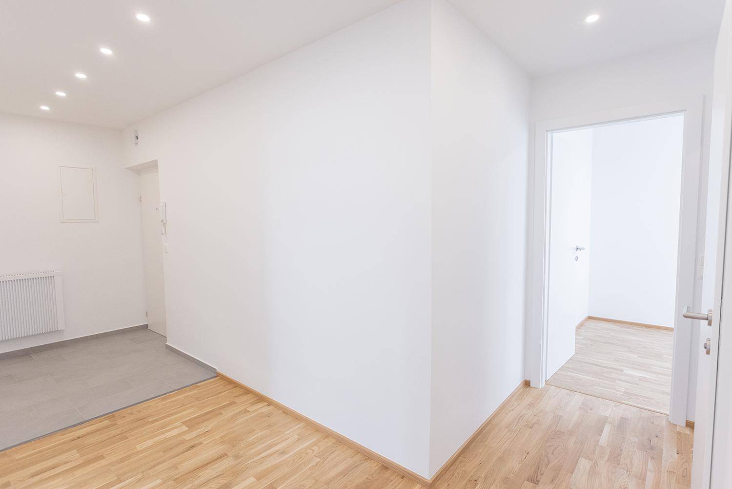 Übergangsbereich zwischen gefliestem Eingang und Flur mit Holzparkett, hell und modern.