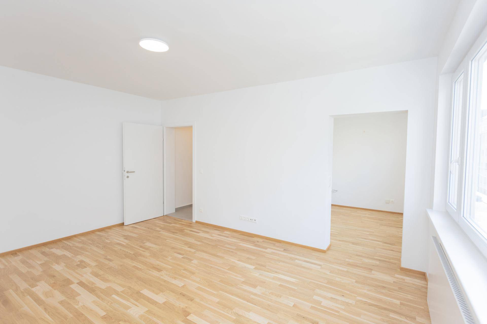 Geräumiger Wohnraum mit Parkettboden und großen Fenstern, bietet viel Platz und Helligkeit.
