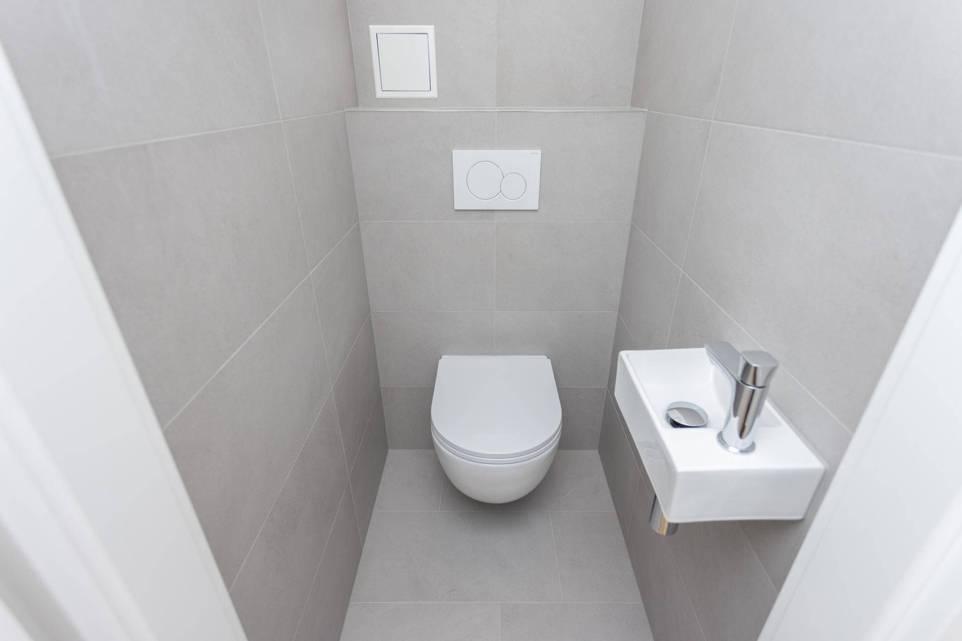 Separates Gäste-WC mit wandhängender Toilette und kleinem Handwaschbecken in modernem Design.