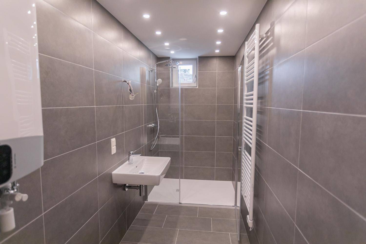 Modernes Badezimmer mit grauen Fliesen, ebenerdiger Dusche und beheiztem Handtuchhalter.