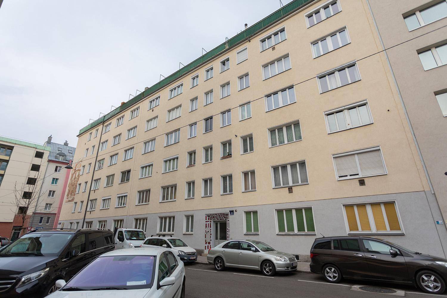 Mehrstöckiges Wohngebäude mit zahlreichen Fenstern und parkenden Autos davor.