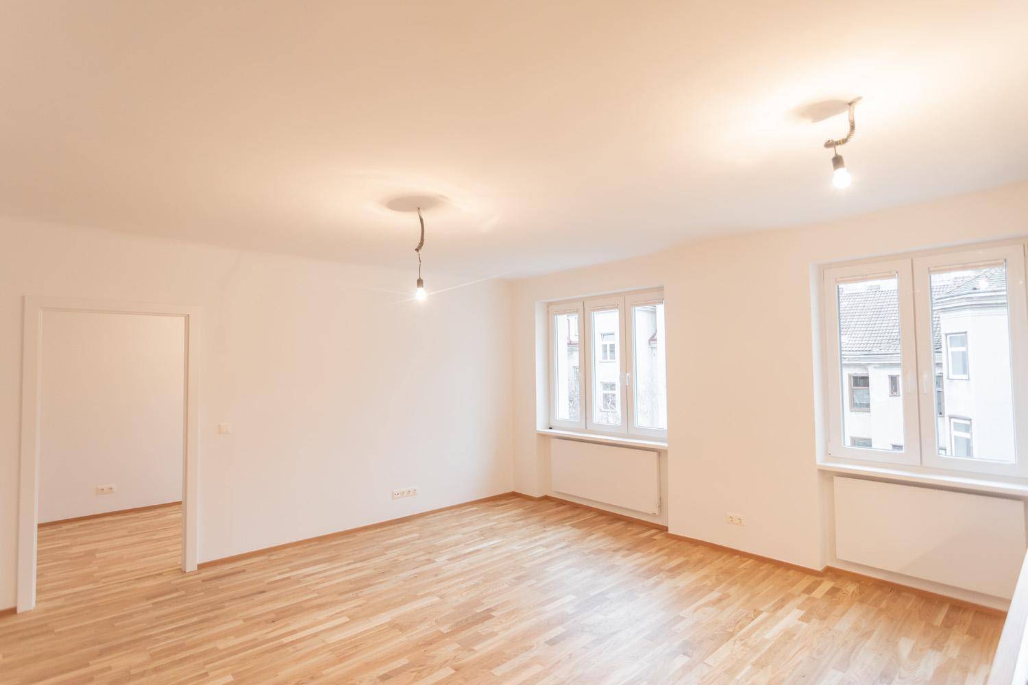 Geräumiges, helles Wohnzimmer mit Parkettboden und großen Fenstern.