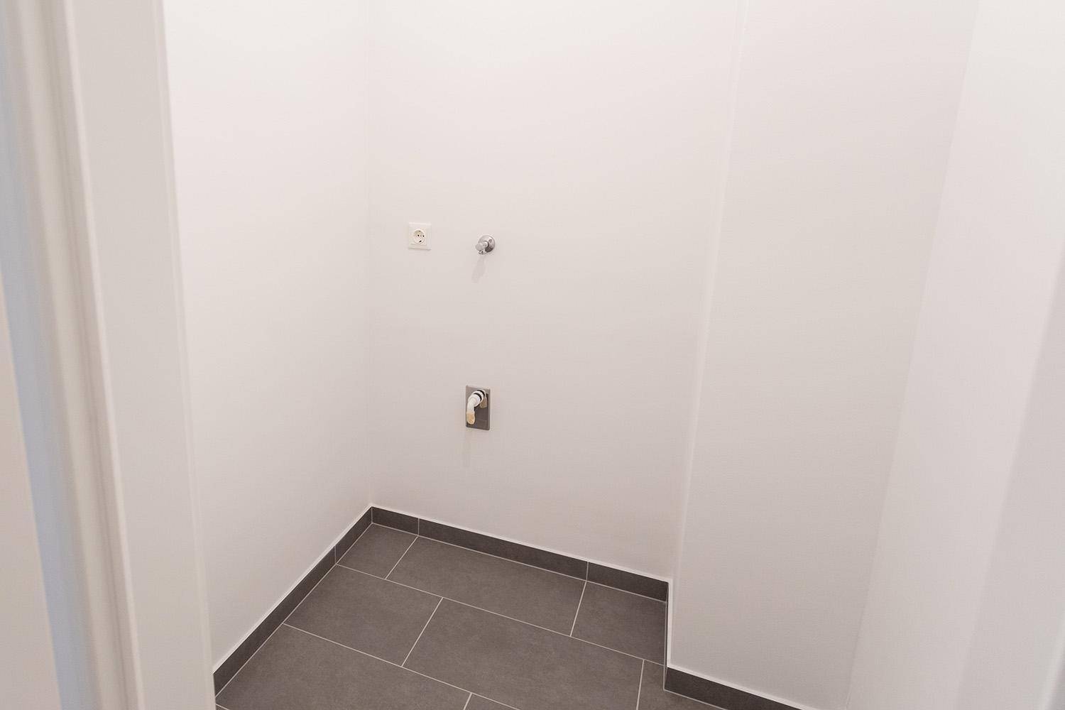 Detailansicht des Hauswirtschaftsraums mit Fliesenboden und Wasseranschlüssen.