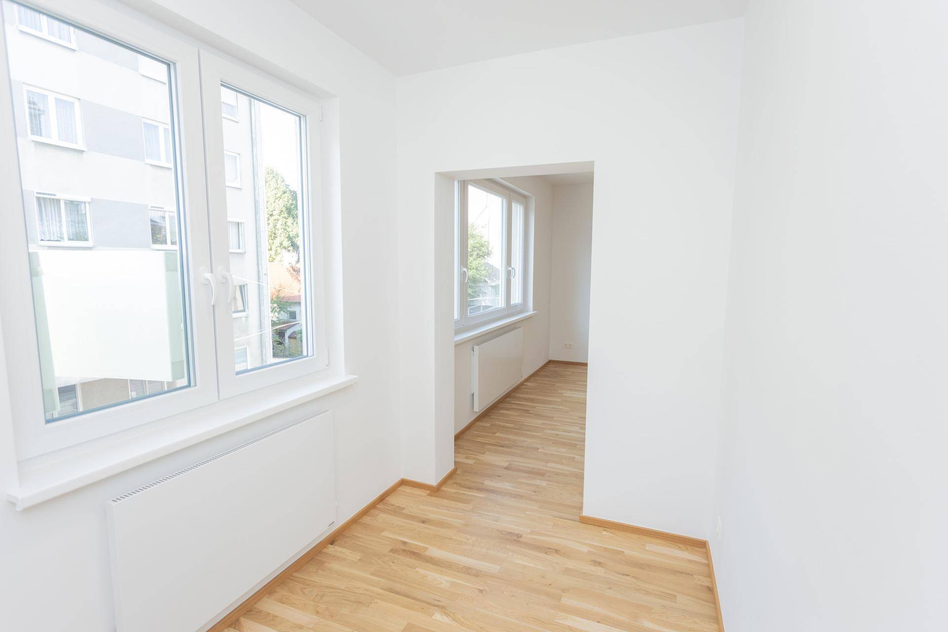 Heller Wohnraum mit Parkettboden und großen Fenstern, die viel Tageslicht hereinlassen.